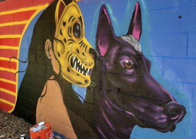 Image of a mural made during Restorative Justice for the Arts' Summer Mural Youth Program. The mural shows a woman wearing a jaguar mask and a dog.