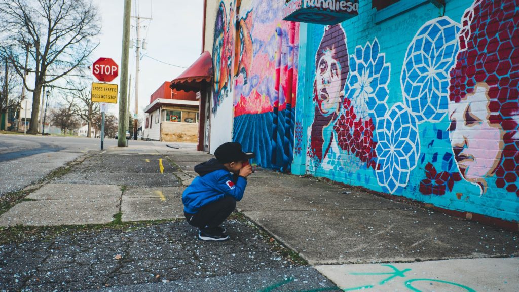 A young boy crouches on a city sidewalk 