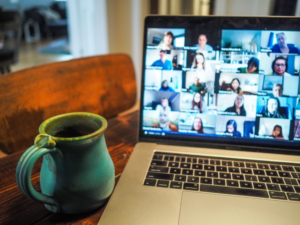 The photo was taken indoors. A silver laptop takes up most of the photo and is open on a wooden table. The computer screen shows a virtual meeting underway with many meeting attendees represented. To the left of the computer, someone has set a ceramic drinking mug that is painted turquoise. Photo by <a href="https://unsplash.com/@cwmonty?utm_source=unsplash&utm_medium=referral&utm_content=creditCopyText">Chris Montgomery</a> on <a href="https://unsplash.com/s/photos/virtual-event?utm_source=unsplash&utm_medium=referral&utm_content=creditCopyText">Unsplash</a> 