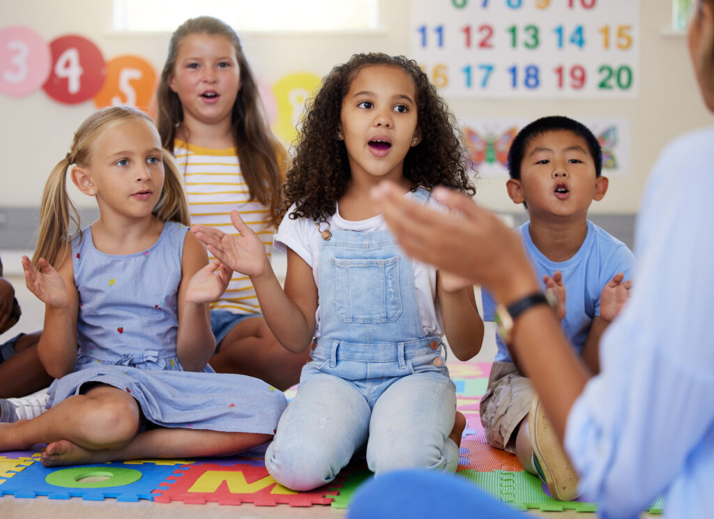 Color photo of a group of kids singing in a classroom.