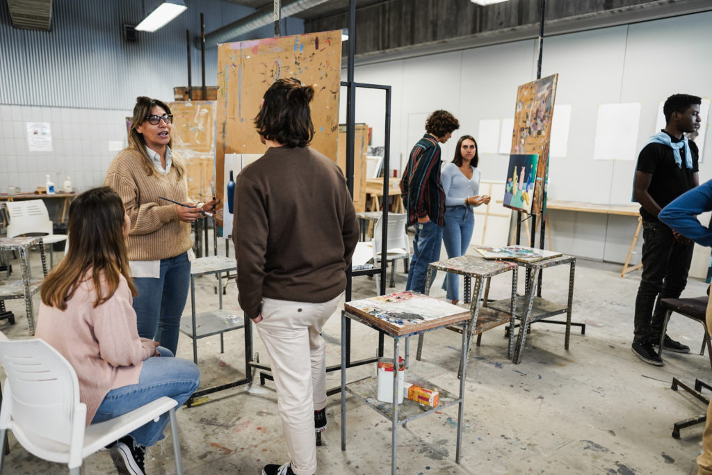 Mature teacher working with art students during painting class at school